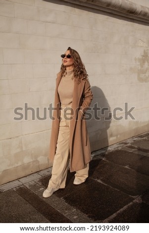 A style woman walking, enjoys a wonderful atmosphere of a vacation in fall time. The girl is wearing a urban beige sweater, sunglasses and resting against the background of the streets of the city Royalty-Free Stock Photo #2193924089