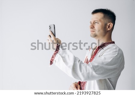 Guy in Ukrainian vyshyvanka stands holding phone, takes selfie and smiles