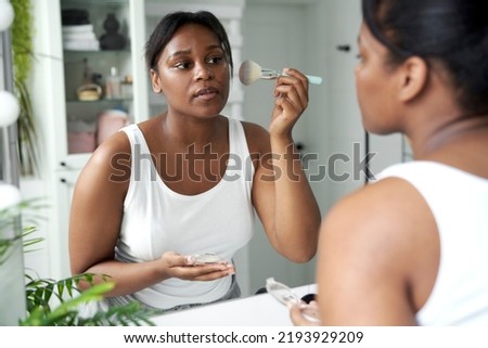 African-American woman applying make up blusher in the bathroom Royalty-Free Stock Photo #2193929209