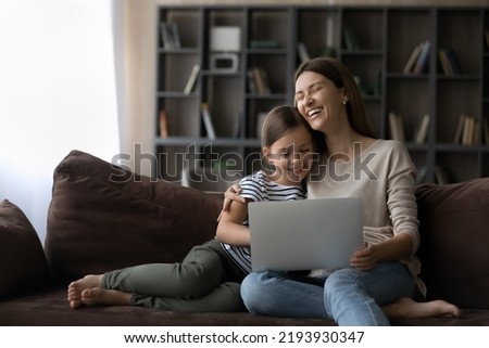 Happy bonding two female generations family watching funny cartoons, film or video in social networks online on computer, having fun spending time together online, resting on cozy sofa at home.