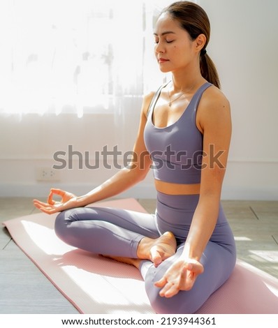 Young beautiful Asian woman sitting on floor in lotus pose, eyes closed practices yoga meditation and breathing exercise for mindfulness. Relaxation and meditation in the morning for healthy lifestyle