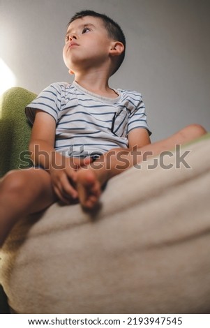 Portrait of an adorable caucasian boy sitting on the sofa at home, looking away attentively. Educational leisure pastime hobby activity. Look at TV screen.