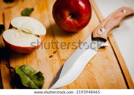 On the wooden kitchen board there is a whole ripe sweet red apple and half an apple, and next to it a sharp kitchen knife. Fruit harvest. Healthy nutrition and vegetarianism. Royalty-Free Stock Photo #2193948465