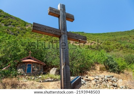 A close-up wooden cross and a view of a small chapel on Mount Ayu-Dag near Hurzuf with a green slope in the background. Big Yalta, Crimea, Ukraine.