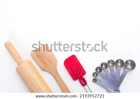 Top view kitchenware wooden rolling pin, wooden spatula, silicone spatula and steel measuring spoons on white background.