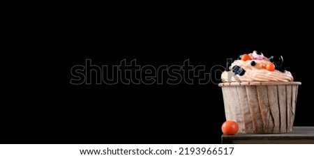Web banner with Halloween cupcake with orange cream and festive sugar sprinkles against the black background. Mockup with copy space