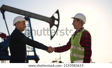 Oil pump. Engineers handshake. Corporate contract. People in helmets work at oil pump. Business contract handshake silhouette. Deposit of minerals. Working engineers teamwork in field at the oil