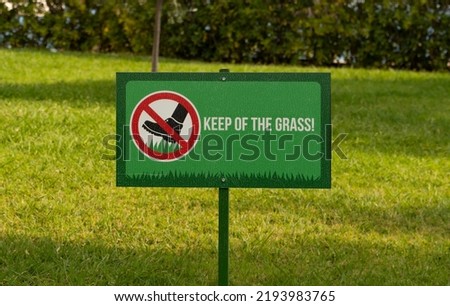 A rectangular sign of green color prohibiting walking on the territory of the lawn against the background of green grass. A sign standing on the lawn and forbids a person to stand on the grass.