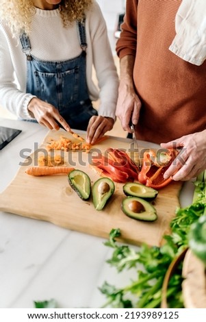 Stock photo of a middle aged woman and man preparing food in a kitchen. They are chopping up some vegetables. They are unrecognizable.