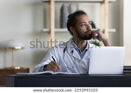 Thoughtful serious male doctor looking at window in office, thinking of patients, future vision, medical career growth, promotion, working at table with laptop, writing records. Royalty-Free Stock Photo #2193995103