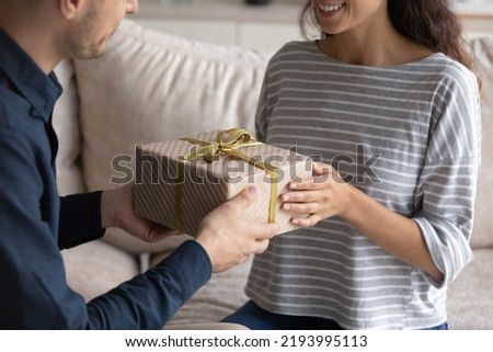 Close up caring young man giving wrapped carboard box to wife, congratulating with happy birthday or special event. Loving sincere millennial generation family couple celebrating wedding anniversary