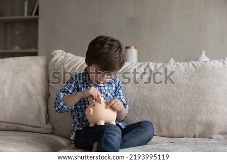 Concentrated little cute kid boy putting coins in piggybank, saving money for future purchase, learning calculating personal budget, accounting or managing finances, education concept. Royalty-Free Stock Photo #2193995119
