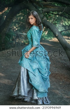 A young woman in a 19th century dress runs away along a forest path, a mystical atmosphere. Historical costume. Woman in a park or forest. Royalty-Free Stock Photo #2193996969