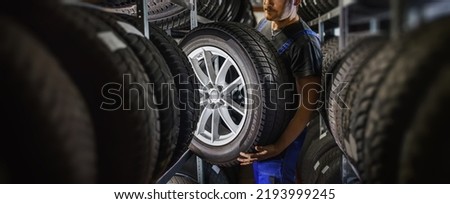 Hardworking experienced worker holding tire and he wants to change it In the tire store. Selective focus on tire. Royalty-Free Stock Photo #2193999245