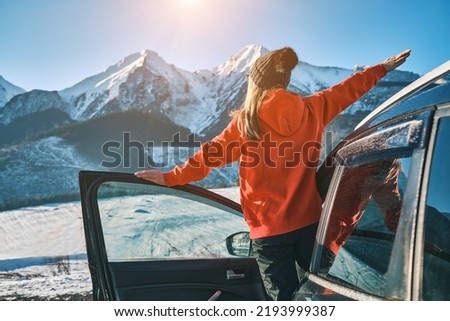 Woman traveling exploring, enjoying the view of the mountains, landscape, lifestyle concept winter vacation outdoors. Female standing near the car in sunny day, travel in the mountains, freedom Royalty-Free Stock Photo #2193999387