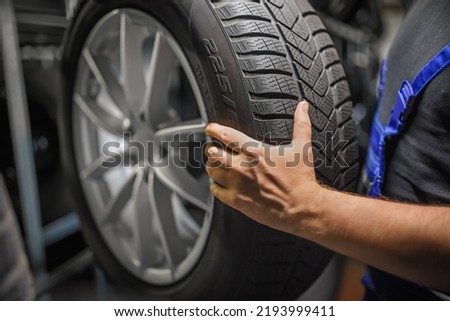 Hardworking experienced worker holding tire and he wants to change it In the tire store. Selective focus on tire. Royalty-Free Stock Photo #2193999411