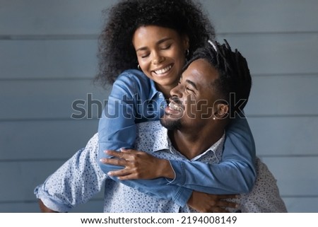 Happy young Brazilian ethnicity man giving piggyback ride to laughing beautiful African American wife, having fun together near grey wall, good trusted family relations, entertainment activity Royalty-Free Stock Photo #2194008149