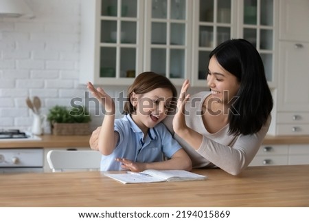 Little cute boy finish schoolwork giving high five to Asian tutor. Loving mother praising her 7s son for good result, well done assignment. Help, symbol of success, teamwork and homeschooling Royalty-Free Stock Photo #2194015869