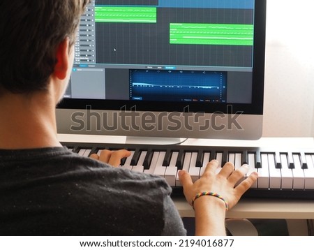 A teenager composing electronic music using a musical keyboard and a computer Royalty-Free Stock Photo #2194016877