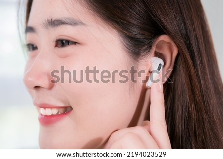 Asian woman use smartphone and wearing earbuds listening music entertainment her enjoy and fun sitting on sofa in living room at home