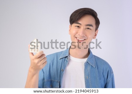 A Young smiling man holding small model house over white background studio	
