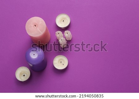 Different types and shapes of candles on a purple background. Top view