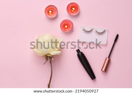 Aroma candle with rose bud and cosmetics on pink background. Romantic, love concept