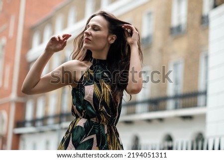 White fashion model posing in front of some London classic buildings. She is wearing a spring dress.