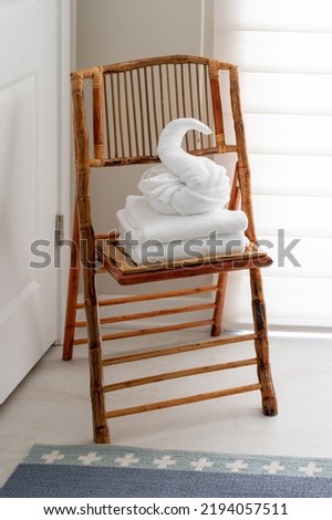 White guest bath towel folded in fancy style in shape of swan sitting atop stack of towels on chair in bed and breakfast hotel bathroom Royalty-Free Stock Photo #2194057511