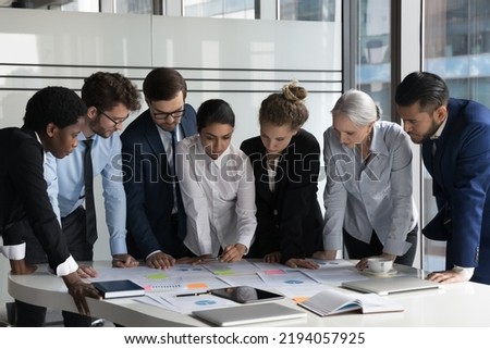Multiethnic business team meeting over project marketing reports, analyzing paper charts with sticky notes, using scrum method, working on strategy, business plan. Diversity, teamwork concept Royalty-Free Stock Photo #2194057925