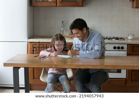 Happy dad and adorable little daughter girl drawing in colored pencils together. Young handsome father and sweet kid enjoying home learning creative activity, making colorful doodles in paper albums