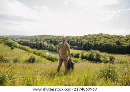 Masculine leisure concept: strong male figure back view with backpack stands on beautiful natural summer landscape outdoors Royalty-Free Stock Photo #2194060969