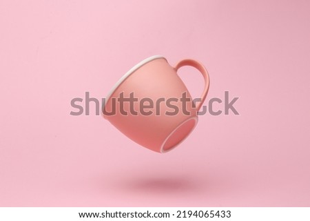 Pink ceramic cup flying in antigravity on pink background with shadow. Levitation object in the air. Creative minimal layout