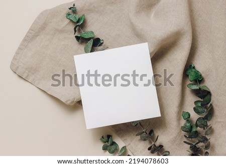 Empty mockup paper card on eucalyptus leaves and linen textile cloth, top view, flat lay. Paper car for brand, social media, business template, greeting and invitation. Minimal boho style