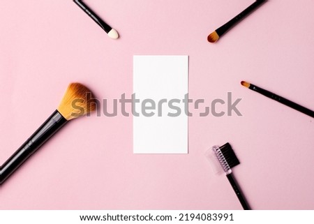 Makeup brush and white business card on pink background. A horizontal template for a makeup artist's business card or flyer design, with copy space