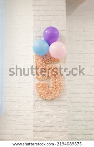 Pink number 5 and balloons are hanging on a white brick wall. The decor of the children's room for the child's birthday