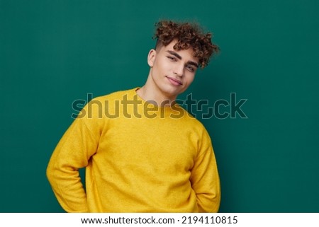 a handsome man stands on a green background in a yellow sweater and smiling pleasantly poses relaxed looking at the camera. Horizontal photo with empty space