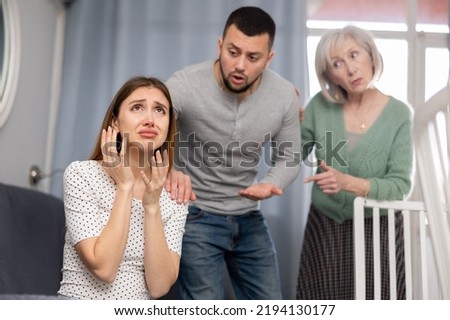 Offended woman sitting on sofa in apartment. Her husband and mother-in-law quarreling with her. Royalty-Free Stock Photo #2194130177