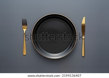Gold knives and forks on a black background, empty black plate. Beautiful gold cutlery. View from above. Royalty-Free Stock Photo #2194136407