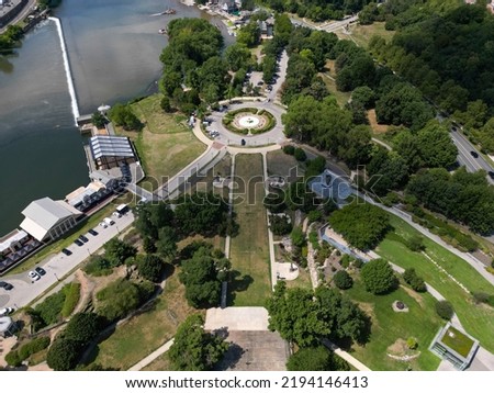 An aerial view of the Fountain of the Sea Horses behind the Museum of Art on a sunny day. The Schuylkill River is calm. The landscape is green and lush but the water fountains are off.