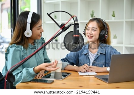 Two millennial Asian female podcaster or radio host enjoys talking and running their podcast together in the studio. podcast or broadcast concept.