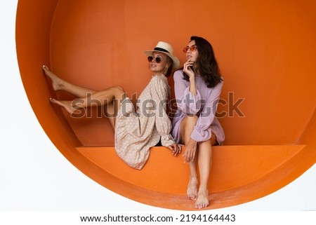Two young beautiful smiling hipster female in trendy summer sundress.Sexy carefree women posing on the street orange background. Positive models having fun Royalty-Free Stock Photo #2194164443