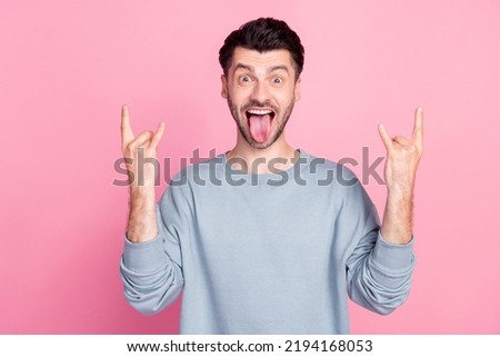 Portrait of overjoyed careless man fingers showing heavy metal symbol tongue out isolated on pink color background