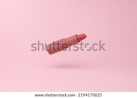 Red lipstick tube flying in antigravity on pink background with shadow. Levitation object in the air. Beauty and fashion concept. Creative minimal layout