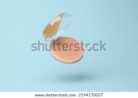 Powder box flying in antigravity on blue background with shadow. Levitation object in the air. Beauty and fashion concept. Creative minimalist layout