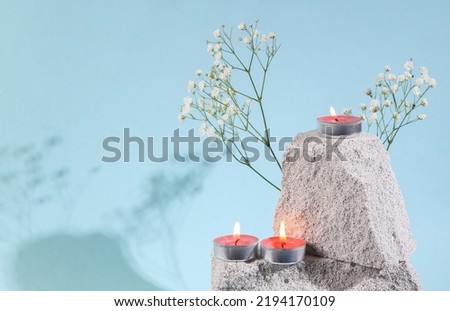 Flaming scented tea candles on stone. Spa, aromatherapy. Blue background. Minimal concept. Aesthetic natural still life