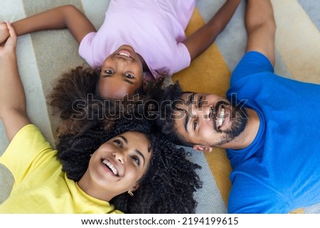 Happy african american family of four bonding lying on bed, black parents and cute little daughter with smiling faces looking at camera in bedroom, mixed race mom dad with child portrait, top view Royalty-Free Stock Photo #2194199615