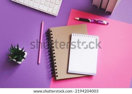 Modern workplace flat lay photography. Paper notebook, pen, pencil, books, plant on a purple table top view
