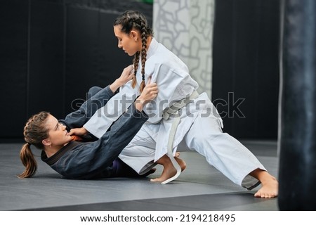 Mma, karate and jiu jitsu with two female athletes practicing, training and sparring in fight class. Healthy, fit and active women in gi or uniform learning self defense for safety and health Royalty-Free Stock Photo #2194218495