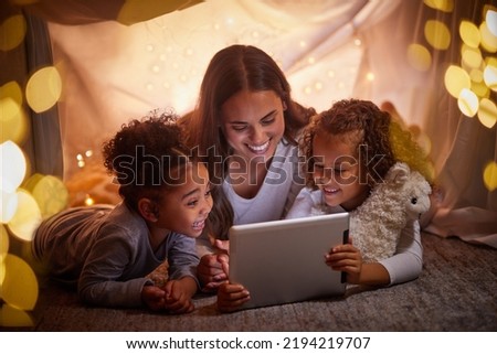 Mother and children live streaming movies on tablet or digital kids app in a tent camping at night and bokeh lights. Care, love mom reading ebook to happy girl or online games with home wifi in dark